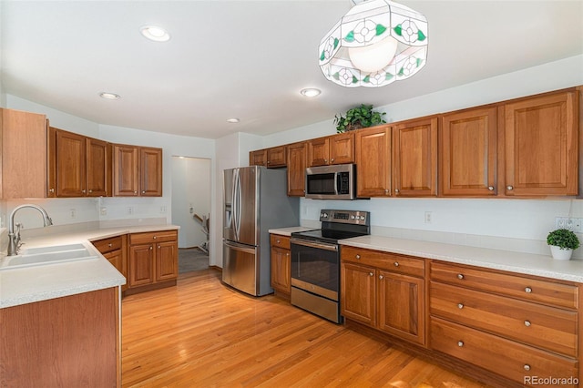 kitchen featuring pendant lighting, sink, stainless steel appliances, and light wood-type flooring