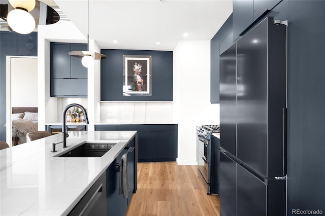 kitchen featuring modern cabinets, pendant lighting, a sink, light wood-style floors, and appliances with stainless steel finishes