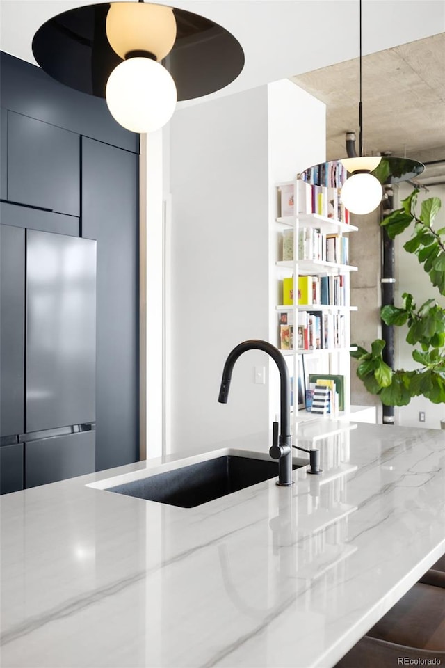 interior space featuring light stone counters, hanging light fixtures, stainless steel fridge, and a sink