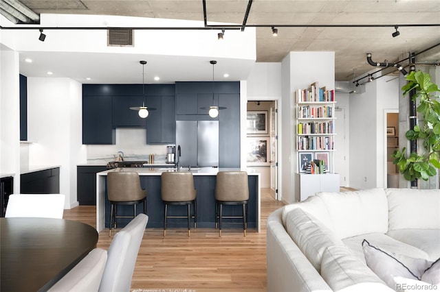 kitchen featuring a breakfast bar area, visible vents, light countertops, stainless steel fridge, and open floor plan