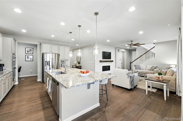 1101 E Witherspoon Dr, Elizabeth, CO 80107 - kitchen featuring a ceiling fan, a sink, stainless steel appliances, a kitchen island with sink, and a glass covered fireplace