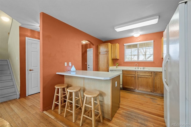 kitchen featuring white appliances, sink, kitchen peninsula, light wood-type flooring, and a breakfast bar