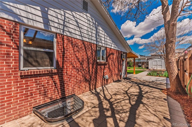 view of side of property featuring brick siding, a storage shed, a patio area, an outbuilding, and fence
