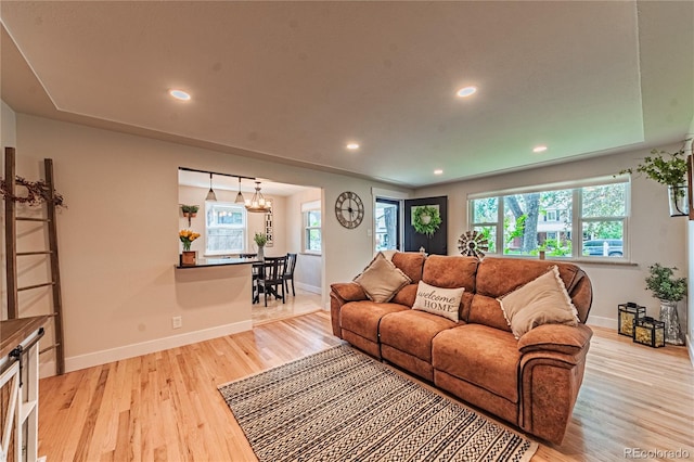 living area with baseboards, healthy amount of natural light, light wood-style flooring, recessed lighting, and a chandelier