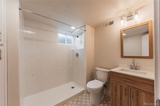 bathroom featuring toilet, tiled shower, and vanity