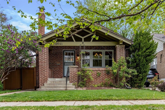 view of front facade featuring brick siding, a chimney, and fence