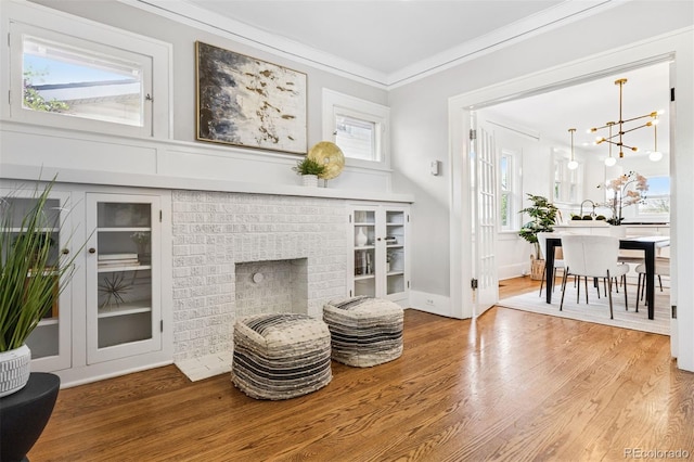 sitting room with a notable chandelier, ornamental molding, built in shelves, wood finished floors, and a fireplace