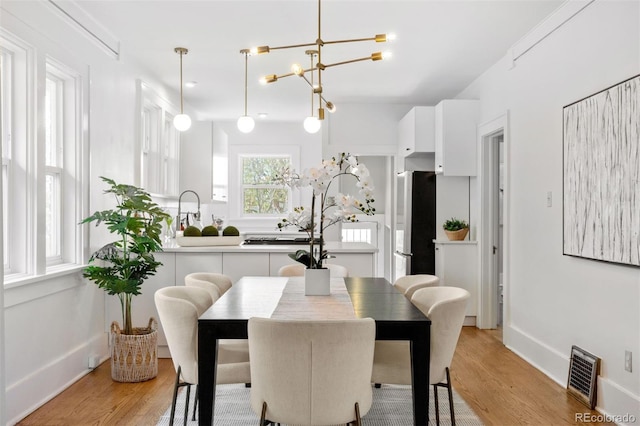 dining space with baseboards, a notable chandelier, light wood-style floors, and visible vents