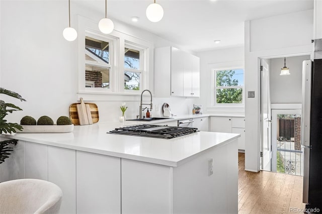 kitchen with light wood-style flooring, gas stovetop, freestanding refrigerator, a sink, and white cabinets
