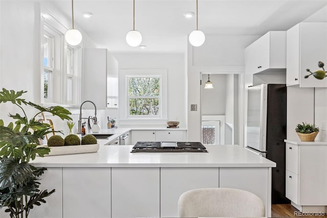 kitchen with a peninsula, a sink, stainless steel appliances, white cabinets, and light countertops