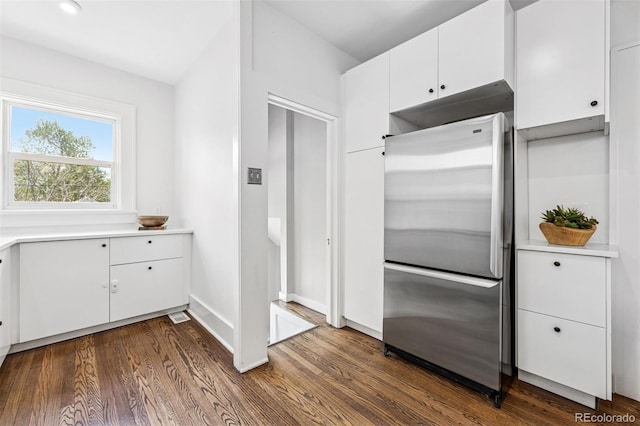 kitchen with stainless steel fridge, white cabinetry, visible vents, light countertops, and dark wood-style floors