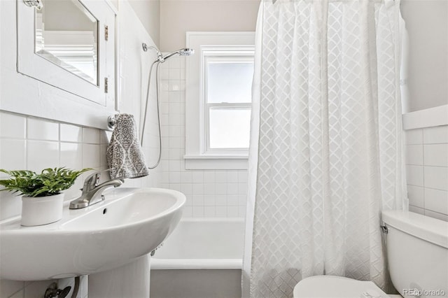 bathroom with a sink, tile walls, shower / bath combo with shower curtain, and toilet