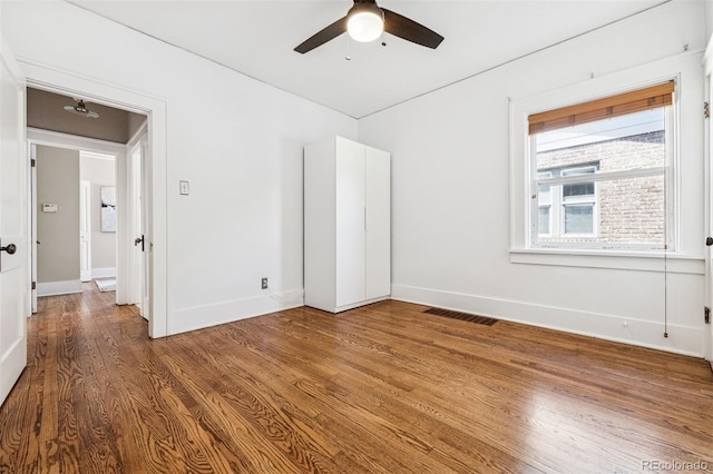 empty room featuring visible vents, wood finished floors, baseboards, and ceiling fan