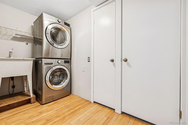 washroom with stacked washer / dryer, laundry area, a sink, and hardwood / wood-style floors