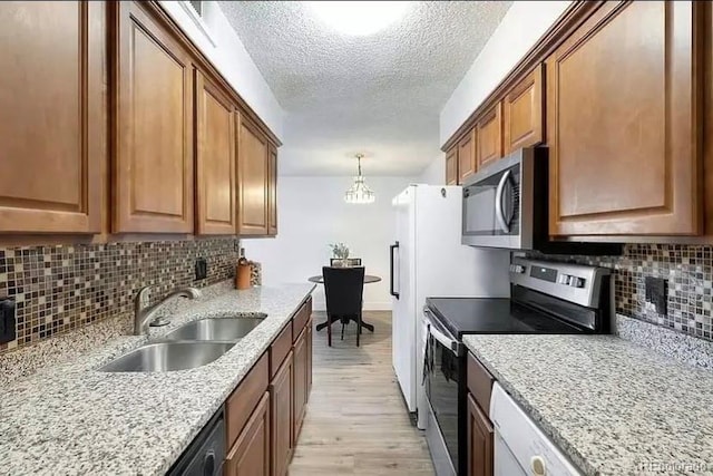 kitchen featuring decorative light fixtures, sink, light stone counters, light hardwood / wood-style floors, and stainless steel appliances