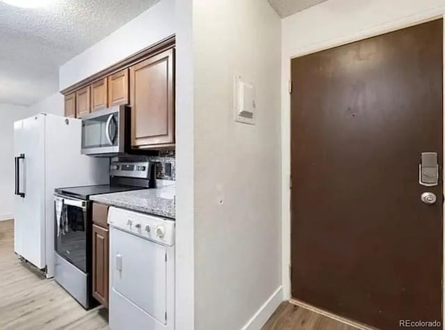 kitchen featuring appliances with stainless steel finishes, light hardwood / wood-style floors, a textured ceiling, and stone counters