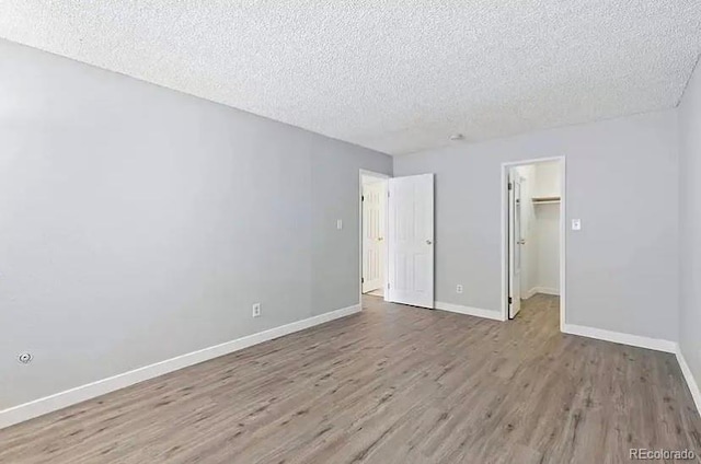 unfurnished bedroom with a walk in closet, wood-type flooring, a closet, and a textured ceiling