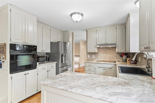 kitchen featuring white cabinetry, sink, backsplash, light stone counters, and black appliances