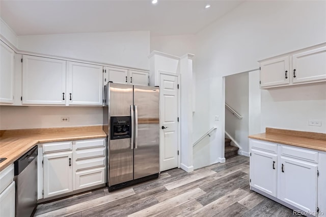 kitchen featuring stainless steel appliances, lofted ceiling, light countertops, light wood-style floors, and white cabinetry