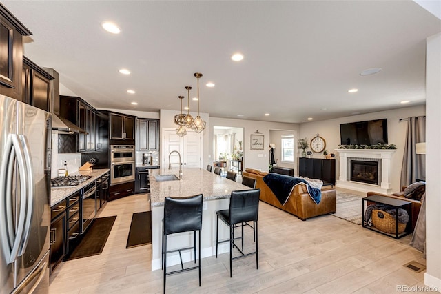 kitchen featuring light hardwood / wood-style floors, pendant lighting, stainless steel appliances, a center island with sink, and sink