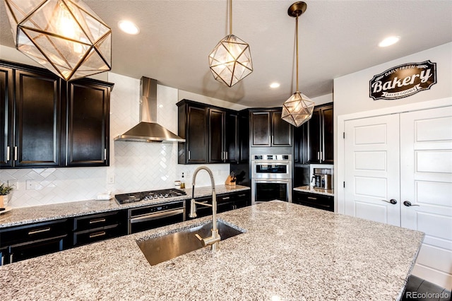 kitchen with light stone counters, tasteful backsplash, decorative light fixtures, wall chimney range hood, and appliances with stainless steel finishes