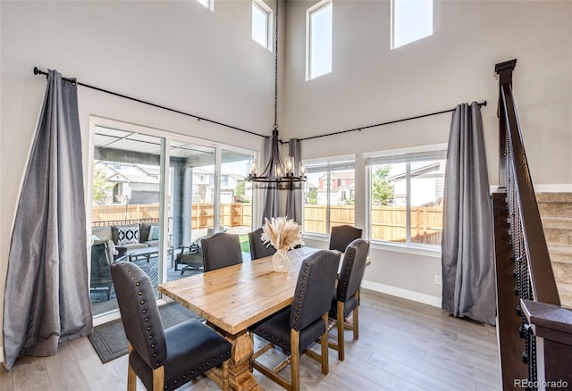 dining area with light wood-type flooring, a high ceiling, and an inviting chandelier