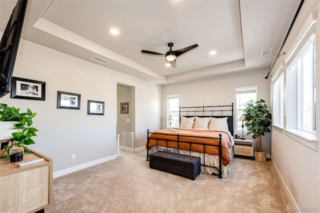 carpeted bedroom featuring multiple windows, a tray ceiling, and ceiling fan