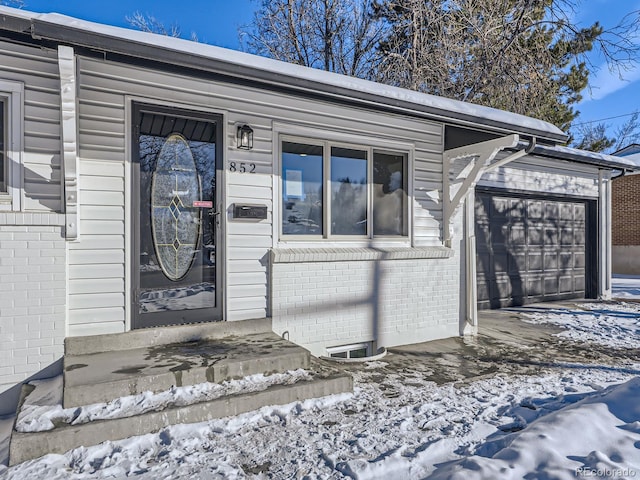 snow covered property entrance featuring a garage