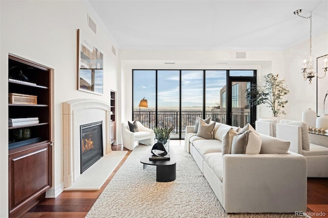 living room with ornamental molding, built in features, dark wood-type flooring, and an inviting chandelier