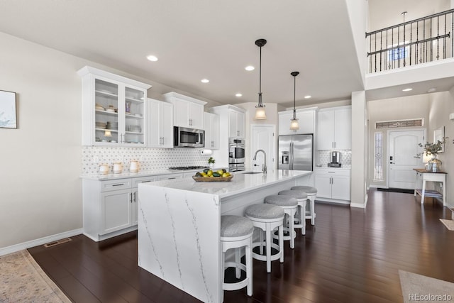 kitchen featuring a kitchen island with sink, appliances with stainless steel finishes, white cabinets, decorative light fixtures, and sink