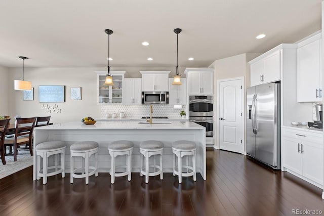 kitchen featuring pendant lighting, stainless steel appliances, a kitchen island with sink, backsplash, and white cabinetry