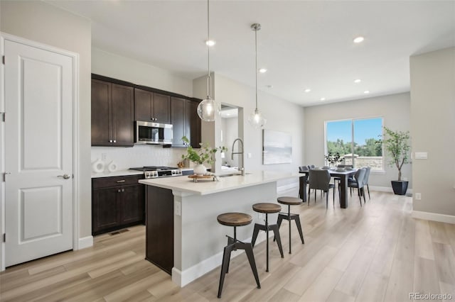 kitchen featuring pendant lighting, sink, dark brown cabinetry, and an island with sink