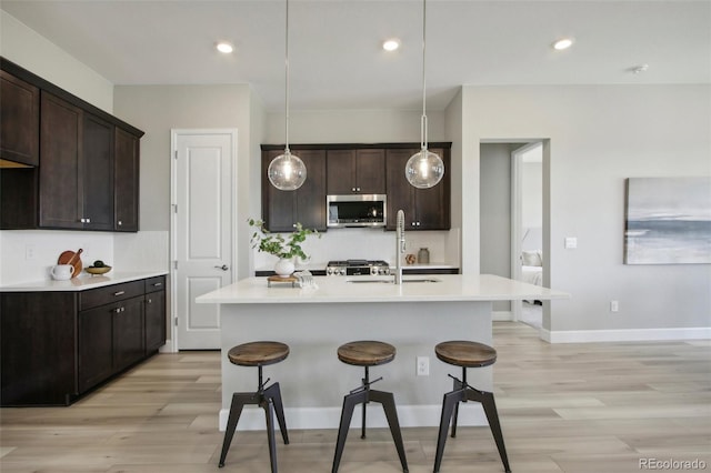 kitchen with dark brown cabinets, a center island with sink, light hardwood / wood-style floors, and decorative light fixtures