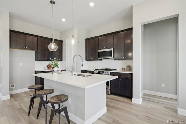 kitchen featuring sink, a kitchen island with sink, dark brown cabinets, stainless steel appliances, and decorative light fixtures