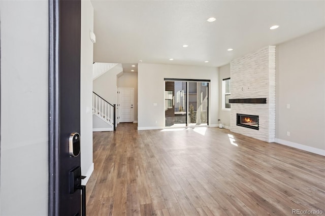 unfurnished living room with recessed lighting, a large fireplace, wood finished floors, baseboards, and stairs