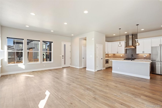 kitchen featuring an island with sink, wall chimney exhaust hood, appliances with stainless steel finishes, light countertops, and white cabinetry