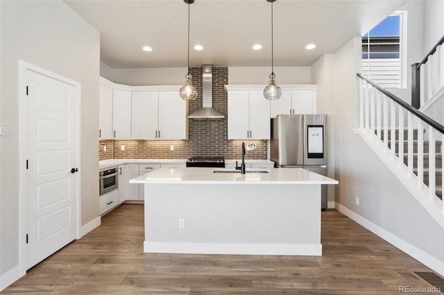 kitchen with light countertops, white cabinetry, a sink, an island with sink, and wall chimney exhaust hood