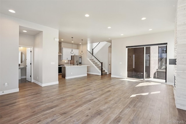 unfurnished living room with stairs, baseboards, wood finished floors, and recessed lighting