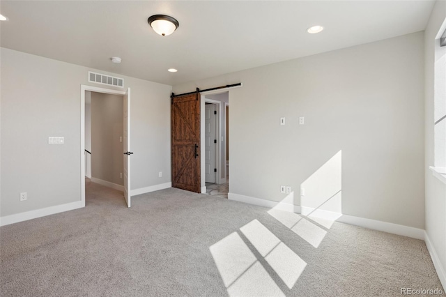 empty room with light colored carpet, visible vents, baseboards, and a barn door