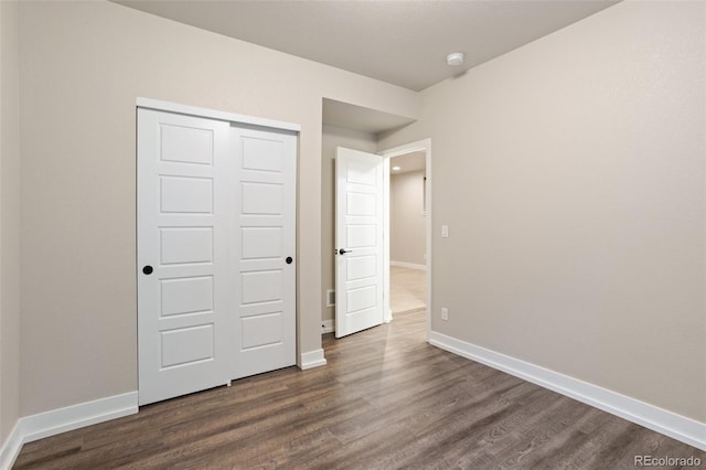 unfurnished bedroom with a closet, baseboards, and dark wood-type flooring