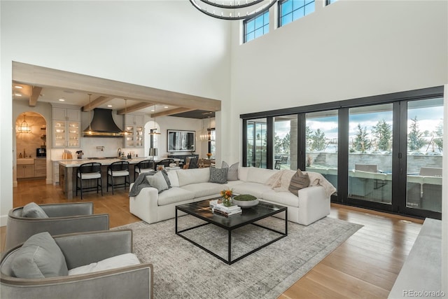 living room with a high ceiling, light wood-type flooring, beam ceiling, and plenty of natural light