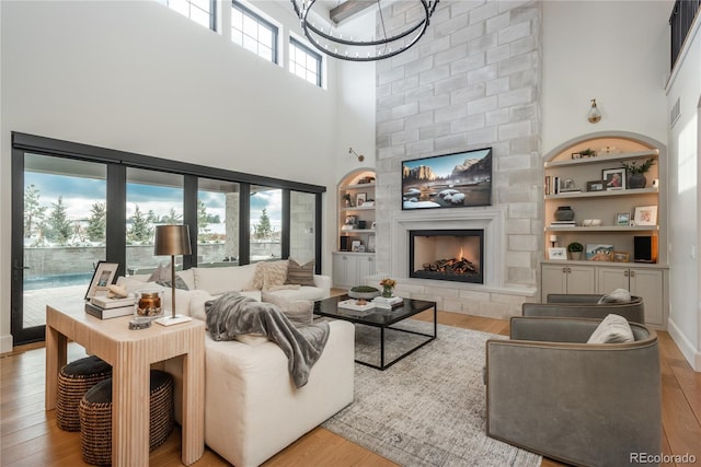 living room with a towering ceiling, light hardwood / wood-style flooring, a fireplace, and built in features