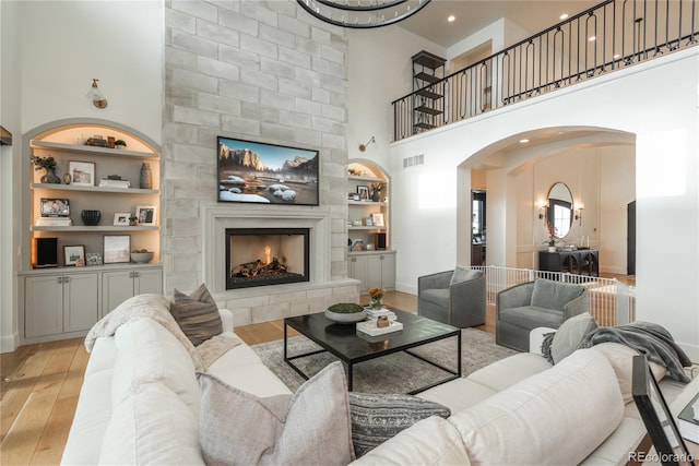 living room featuring a high ceiling, built in shelves, light hardwood / wood-style floors, and a fireplace