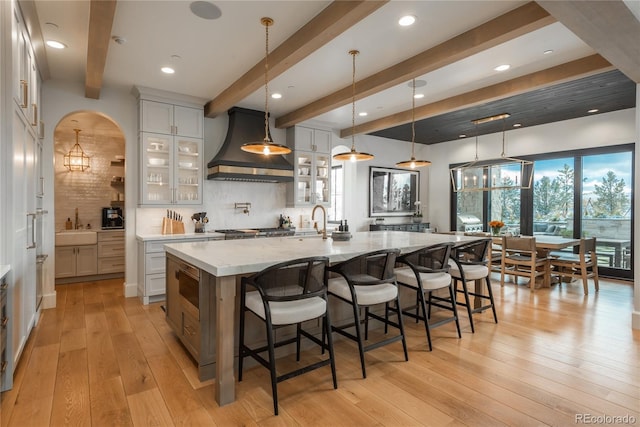 kitchen with white cabinetry, backsplash, decorative light fixtures, custom exhaust hood, and a spacious island