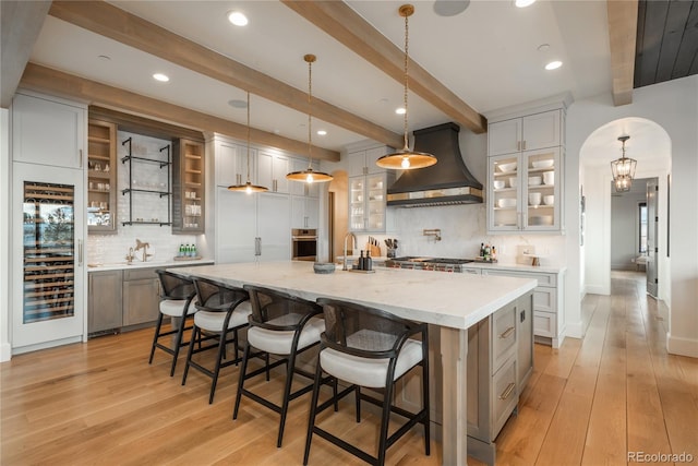 kitchen featuring a spacious island, hanging light fixtures, custom exhaust hood, and beam ceiling