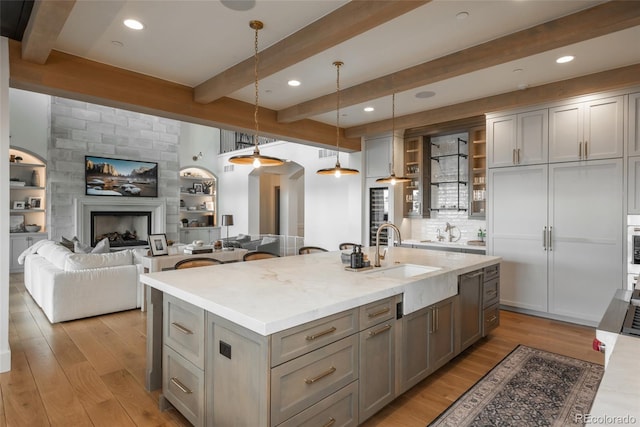 kitchen with sink, gray cabinetry, an island with sink, beam ceiling, and decorative light fixtures