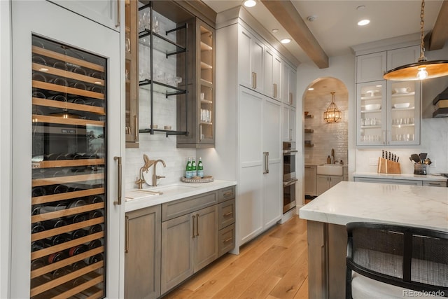 bar featuring backsplash, light stone countertops, pendant lighting, light wood-type flooring, and wine cooler