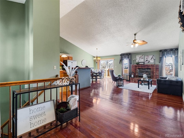 living room with lofted ceiling, hardwood / wood-style flooring, a textured ceiling, a brick fireplace, and ceiling fan with notable chandelier