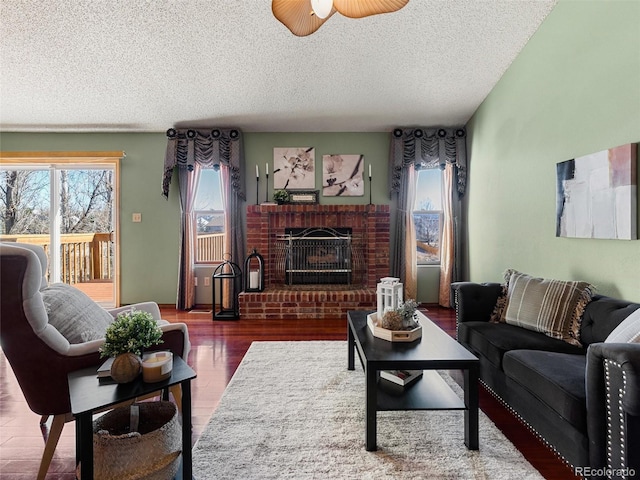 living room featuring a brick fireplace, ceiling fan, a textured ceiling, and wood finished floors