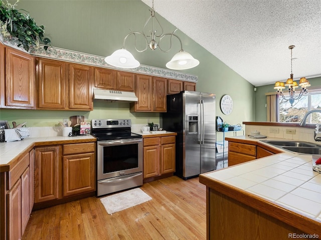 kitchen with tile counters, appliances with stainless steel finishes, an inviting chandelier, under cabinet range hood, and a sink